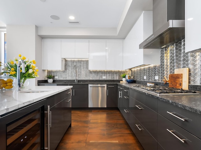 kitchen featuring wine cooler, dark stone counters, white cabinetry, wall chimney range hood, and appliances with stainless steel finishes