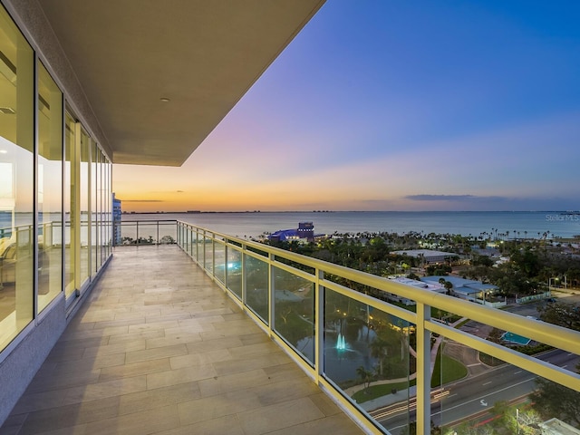 balcony at dusk featuring a water view