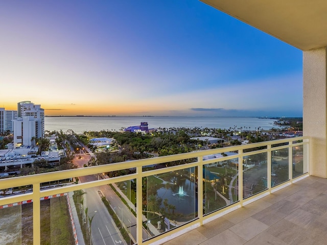 balcony at dusk featuring a water view