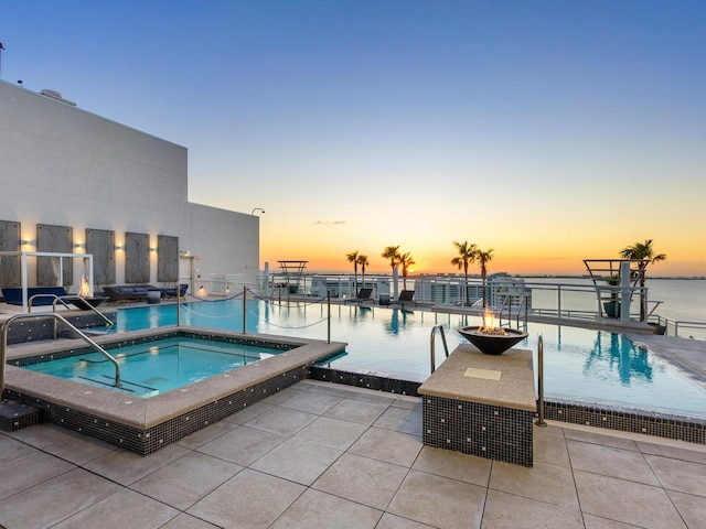 pool at dusk with a community hot tub, a patio, and a water view