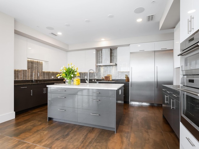 kitchen featuring dark hardwood / wood-style flooring, white cabinets, tasteful backsplash, wall chimney range hood, and appliances with stainless steel finishes