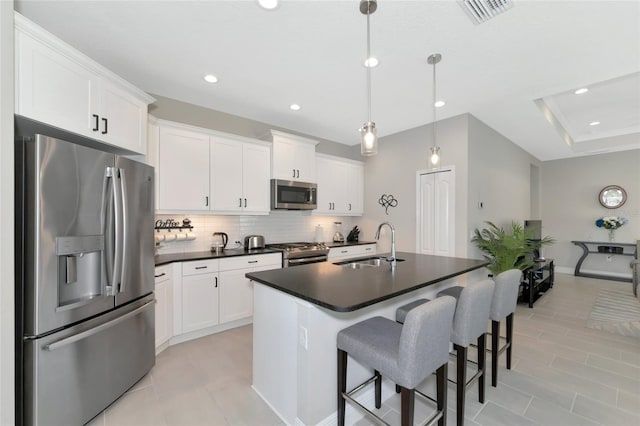 kitchen with a center island with sink, white cabinetry, stainless steel appliances, and hanging light fixtures