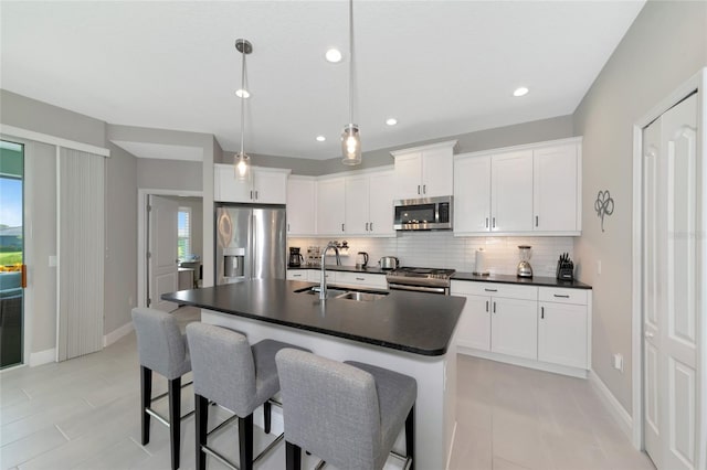 kitchen with appliances with stainless steel finishes, a kitchen island with sink, sink, pendant lighting, and white cabinets