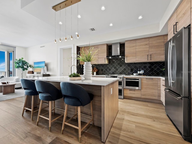 kitchen featuring light wood-type flooring, appliances with stainless steel finishes, wall chimney exhaust hood, and a breakfast bar