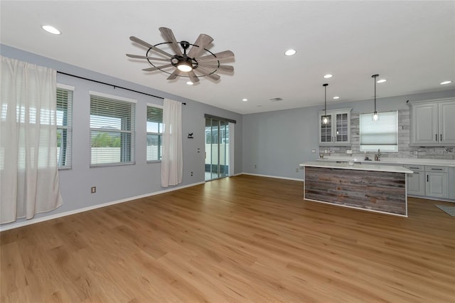 kitchen with a kitchen island, backsplash, gray cabinets, hanging light fixtures, and light hardwood / wood-style floors