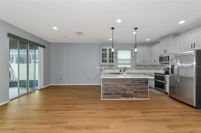 kitchen featuring light hardwood / wood-style floors, backsplash, pendant lighting, appliances with stainless steel finishes, and white cabinetry