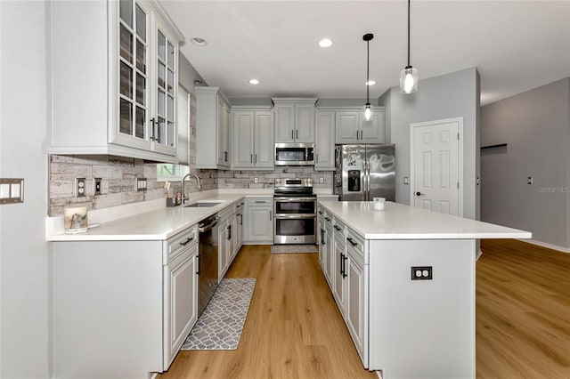 kitchen with light hardwood / wood-style floors, stainless steel appliances, a center island, hanging light fixtures, and sink