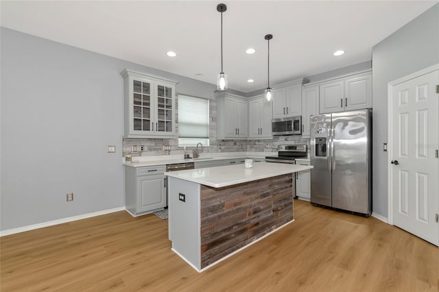 kitchen featuring stainless steel appliances, sink, decorative light fixtures, a kitchen island, and light wood-type flooring