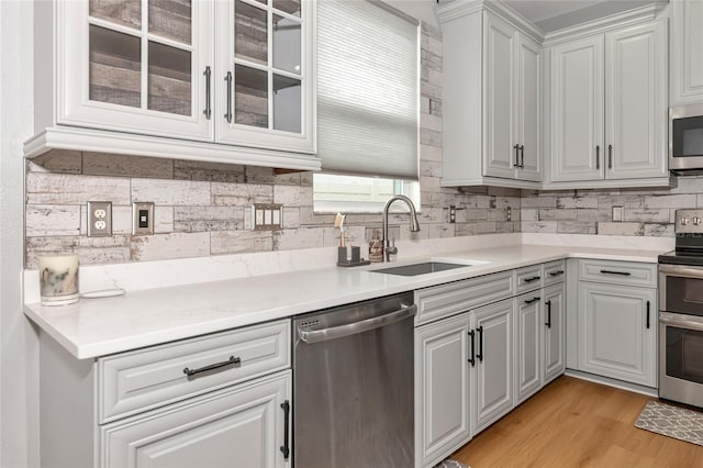 kitchen with tasteful backsplash, white cabinetry, appliances with stainless steel finishes, sink, and light hardwood / wood-style floors