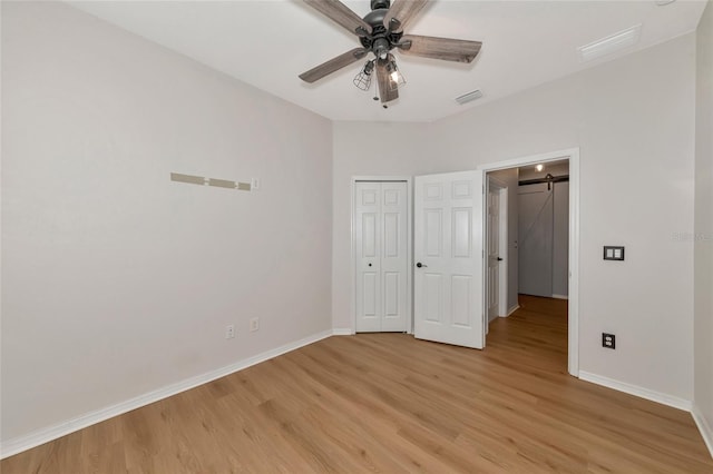 unfurnished bedroom with a barn door, ceiling fan, a closet, and light wood-type flooring