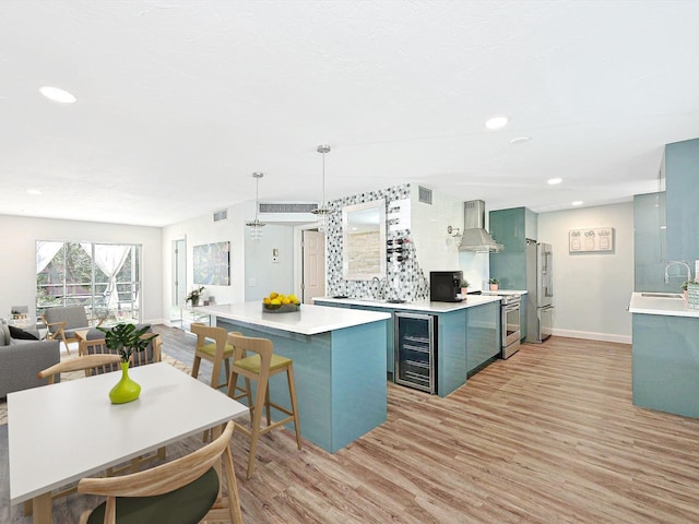 kitchen featuring appliances with stainless steel finishes, pendant lighting, sink, beverage cooler, and wall chimney range hood