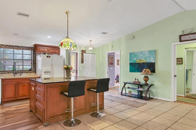 kitchen with lofted ceiling, a center island, sink, white refrigerator with ice dispenser, and a breakfast bar