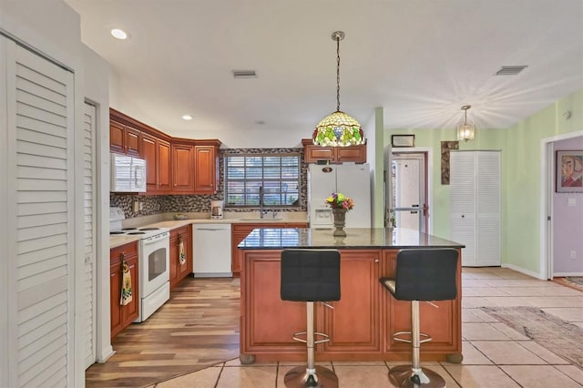 kitchen with white appliances, a breakfast bar area, light tile patterned floors, and a center island