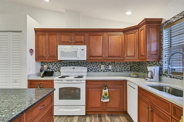 kitchen featuring vaulted ceiling, sink, tasteful backsplash, white appliances, and dark stone countertops