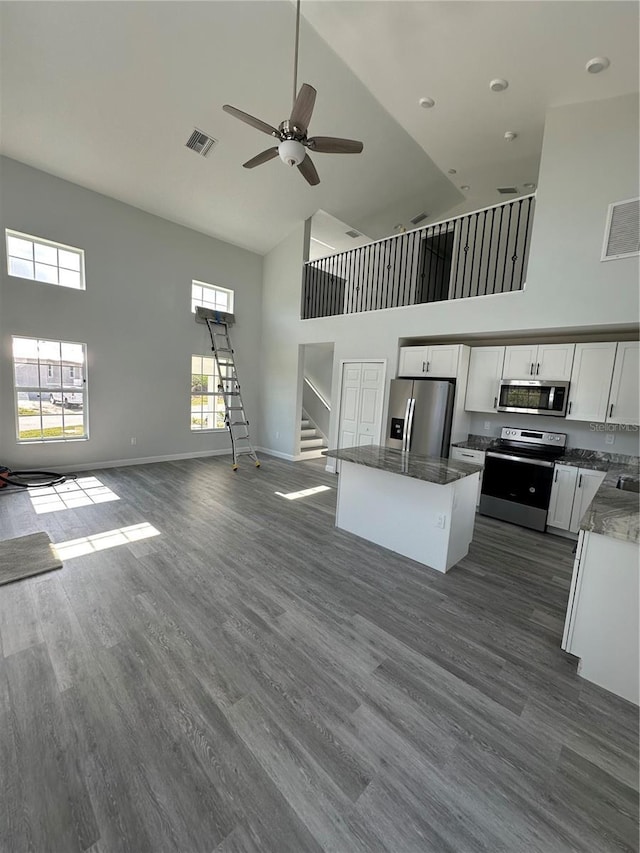 kitchen featuring dark wood-type flooring, white cabinetry, stainless steel appliances, a high ceiling, and a kitchen island