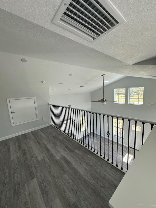 corridor with dark hardwood / wood-style flooring, vaulted ceiling, and a textured ceiling