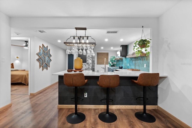 kitchen featuring kitchen peninsula, backsplash, a breakfast bar, wall chimney range hood, and wood-type flooring