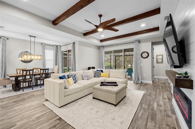 living room with ceiling fan with notable chandelier, a tray ceiling, and light hardwood / wood-style flooring