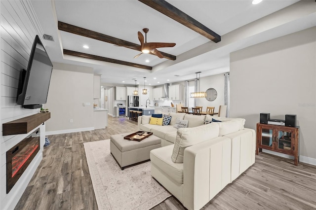 living room with beam ceiling, ceiling fan, sink, light hardwood / wood-style flooring, and a tray ceiling