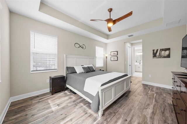 bedroom with hardwood / wood-style flooring, ceiling fan, a tray ceiling, and ensuite bathroom