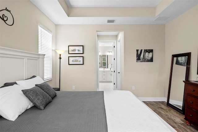 bedroom featuring ensuite bathroom, wood-type flooring, and a tray ceiling