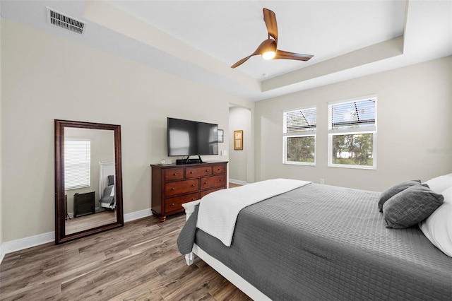 bedroom with hardwood / wood-style floors, ceiling fan, and a raised ceiling