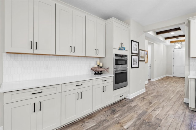 kitchen with light hardwood / wood-style flooring, beamed ceiling, double oven, backsplash, and white cabinets