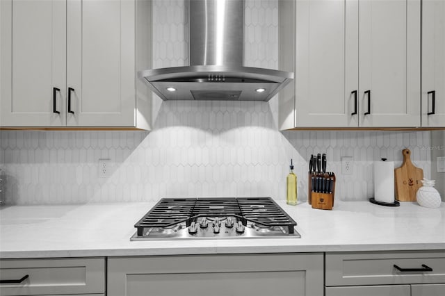 kitchen with stainless steel gas stovetop, decorative backsplash, light stone counters, and wall chimney range hood