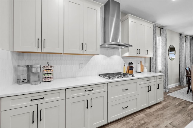 kitchen featuring white cabinetry, wall chimney exhaust hood, tasteful backsplash, stainless steel gas stovetop, and light wood-type flooring