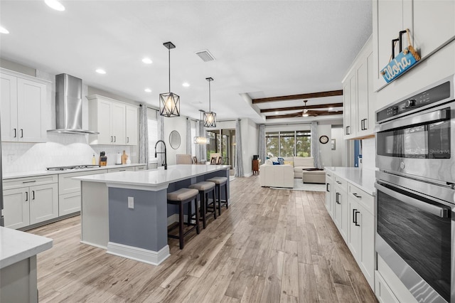 kitchen featuring light hardwood / wood-style flooring, white cabinets, wall chimney range hood, and appliances with stainless steel finishes