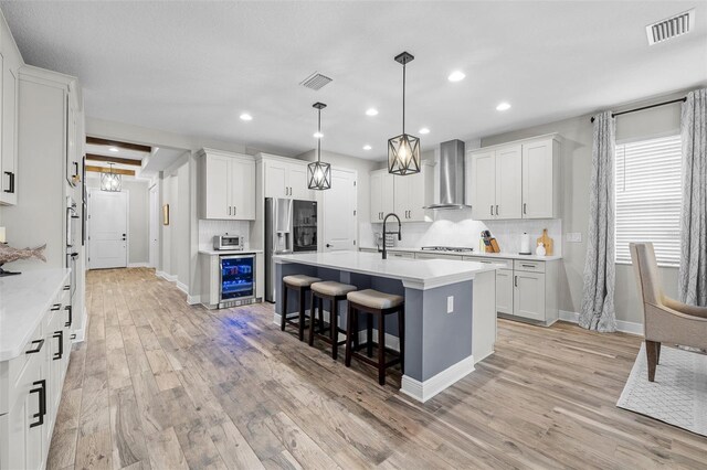 kitchen featuring stainless steel fridge, white cabinets, and wall chimney range hood