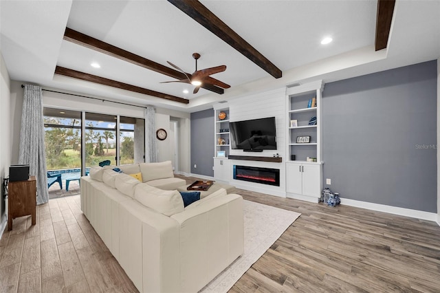 living room featuring a large fireplace, a raised ceiling, ceiling fan, beamed ceiling, and light hardwood / wood-style floors