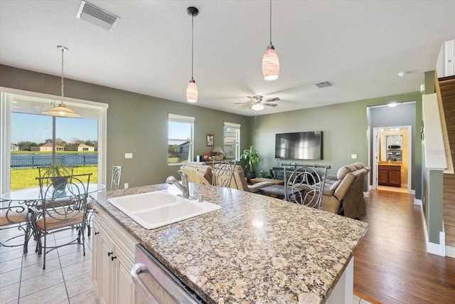 kitchen with sink, an island with sink, stainless steel dishwasher, light wood-type flooring, and decorative light fixtures