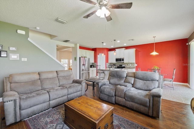 living room with a textured ceiling, hardwood / wood-style floors, and ceiling fan