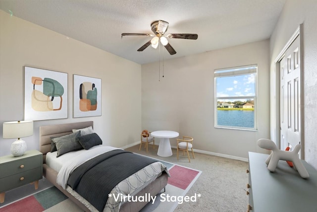 carpeted bedroom with ceiling fan, a textured ceiling, a closet, and a water view