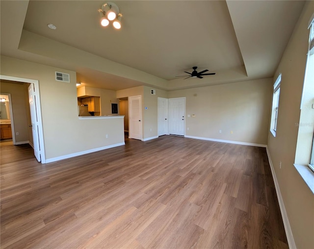 unfurnished living room featuring hardwood / wood-style flooring, ceiling fan, and a raised ceiling