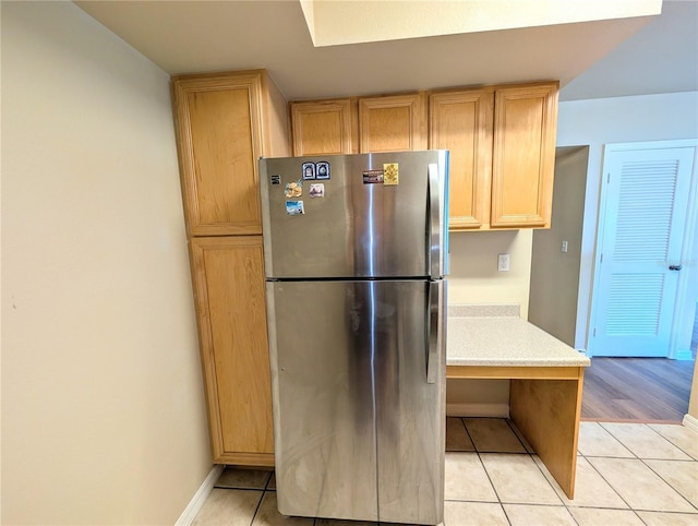 kitchen with light brown cabinets, stainless steel refrigerator, and light tile patterned flooring