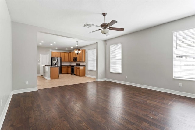 unfurnished living room with light hardwood / wood-style floors, a healthy amount of sunlight, and ceiling fan with notable chandelier