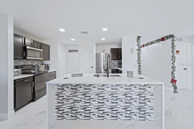 kitchen featuring stainless steel appliances, sink, backsplash, dark brown cabinets, and a kitchen island with sink