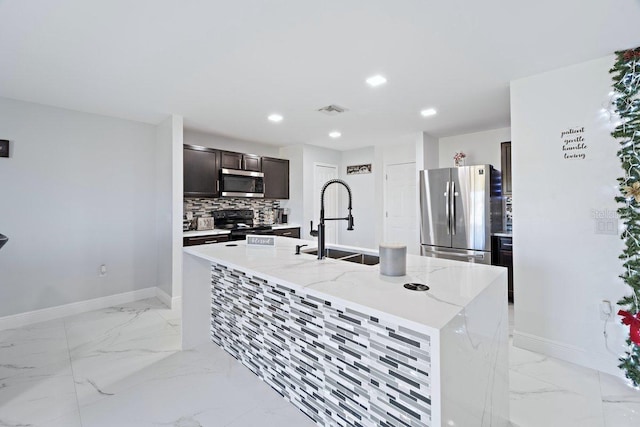 kitchen featuring a center island with sink, dark brown cabinetry, sink, light stone countertops, and appliances with stainless steel finishes