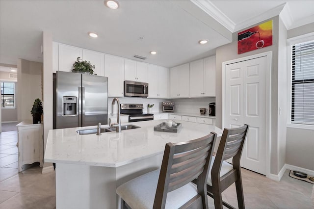 kitchen with sink, appliances with stainless steel finishes, light stone countertops, an island with sink, and crown molding