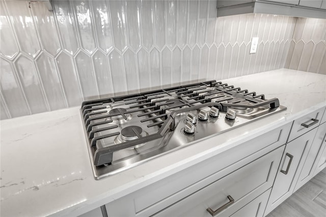 interior details with light stone counters, stainless steel gas cooktop, and backsplash