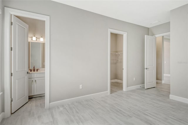 unfurnished bedroom featuring connected bathroom, a spacious closet, a closet, and light hardwood / wood-style flooring