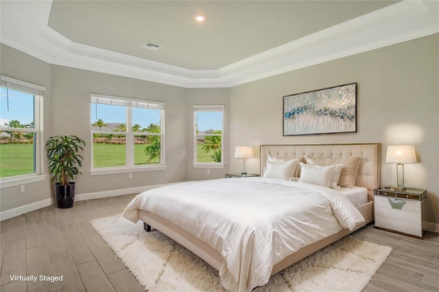 bedroom with crown molding, light hardwood / wood-style flooring, and a tray ceiling