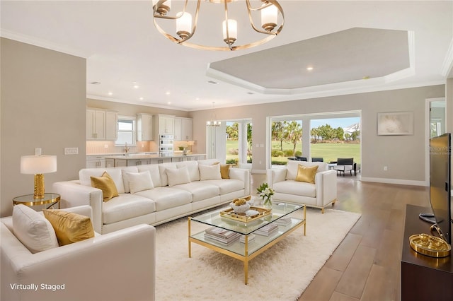 living room featuring a raised ceiling, crown molding, a chandelier, and light hardwood / wood-style floors