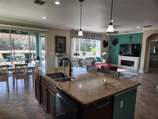 kitchen featuring crown molding, a textured ceiling, decorative light fixtures, sink, and an island with sink