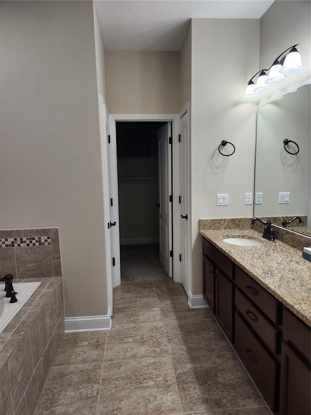 bathroom with vanity, a textured ceiling, and a relaxing tiled tub