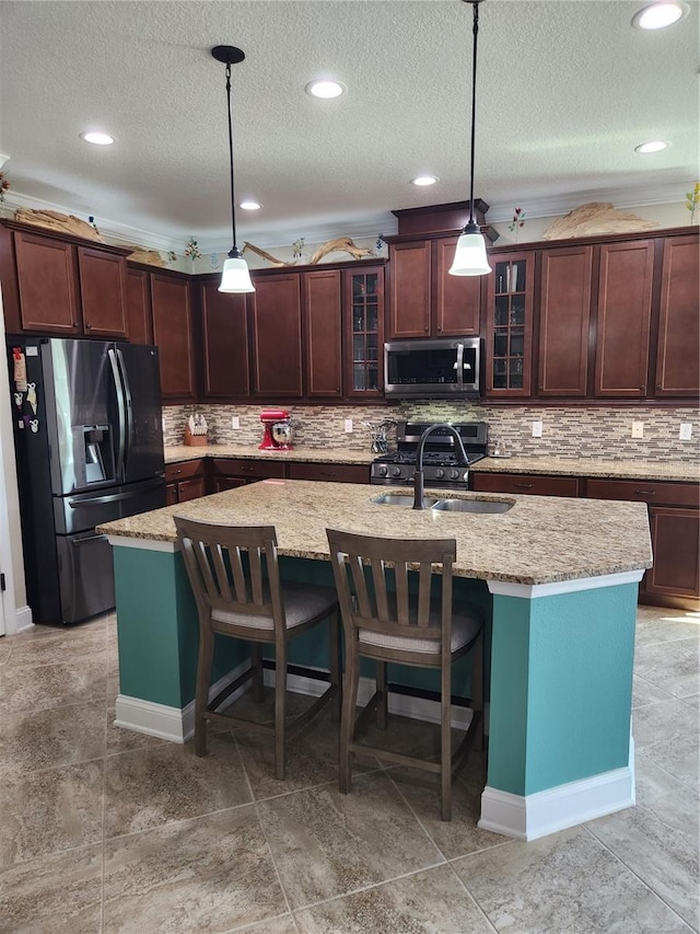 kitchen with light stone counters, a center island with sink, stainless steel appliances, a textured ceiling, and pendant lighting