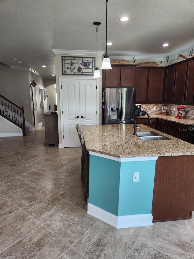 kitchen featuring a center island with sink, stainless steel refrigerator with ice dispenser, dark brown cabinetry, hanging light fixtures, and sink