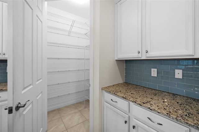 kitchen with white cabinets, light tile patterned floors, backsplash, and light stone counters